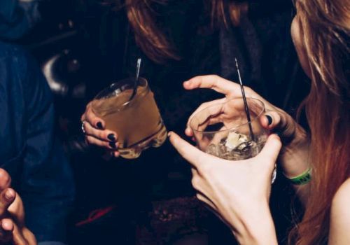 The image shows several people holding drinks and interacting closely in what appears to be a lively social gathering or party setting.
