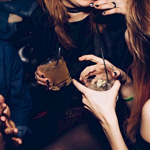 The image shows several people holding drinks and interacting closely in what appears to be a lively social gathering or party setting.