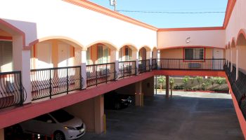 An exterior view of a motel or apartment complex with a courtyard, featuring two stories, balconies, and parked cars.