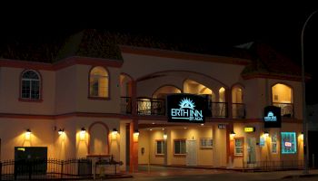 A building at night with a lit sign that reads "ERTH INN by AGA," featuring arched windows, balconies, and multiple lights illuminating the facade.