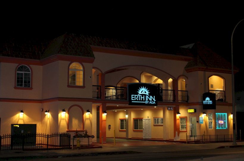 A building at night with a lit sign that reads "ERTH INN by AGA," featuring arched windows, balconies, and multiple lights illuminating the facade.