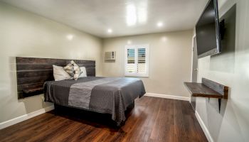 A modern bedroom with a large bed, wall-mounted TV, wooden floor, and minimalistic decor, including pillows and a small table.