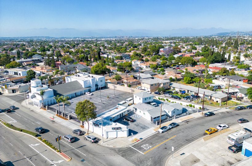 An aerial view of an urban neighborhood with residential buildings, a church with a dome, streets with cars, and distant mountains in the background.