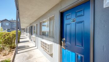 A blue door with the number 109 leads to a row of similar doors along a walkway in a residential or hotel complex.