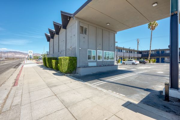 A modern, concrete building with unique roof design, trimmed shrubs, parking lot, and a clear sidewalk under a blue sky ends the sentence.