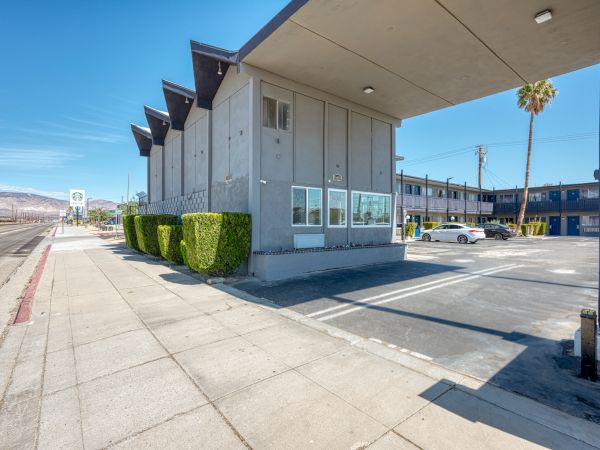 A modern, concrete building with unique roof design, trimmed shrubs, parking lot, and a clear sidewalk under a blue sky ends the sentence.