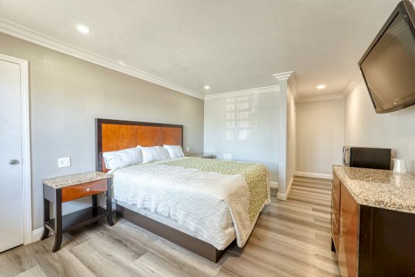 A neatly arranged hotel room with a bed, nightstand, TV, microwave, and dresser; the room has modern decor and lighting.