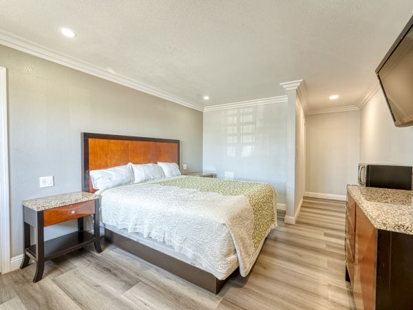 A neatly arranged hotel room with a bed, nightstand, TV, microwave, and dresser; the room has modern decor and lighting.