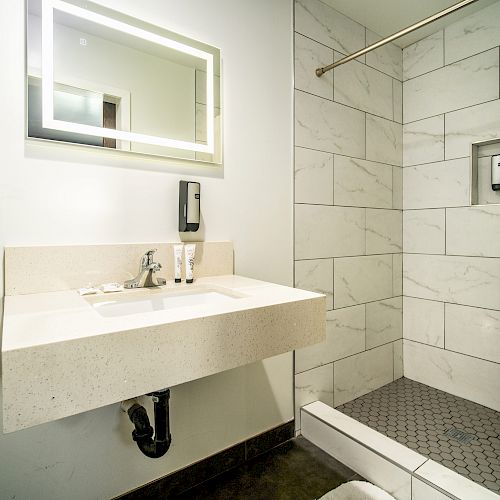 A modern bathroom with a wall-mounted sink, a large mirror, and a walk-in shower with white tiles and a shower curtain.