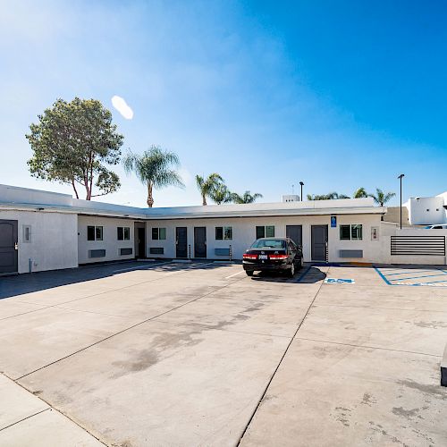 A small, white, single-story building with several units, a parking lot with one parked car, and the number 5807 visible on the right.