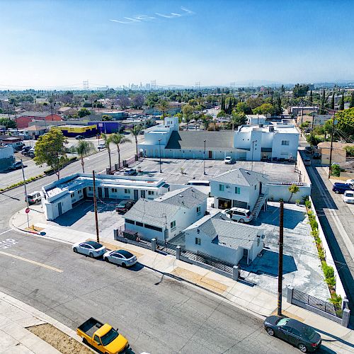 The image shows an aerial view of a residential neighborhood with houses, parked cars, trees, and clear skies in the background.