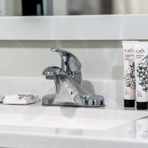 A bathroom sink with a chrome faucet and two tubes of Cava lotion on the right, along with soap placed on the left.