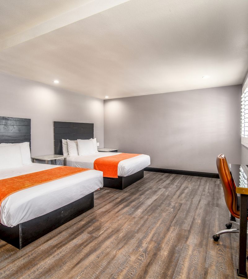 A wide view of a hotel room with two beds, a desk, and a window.