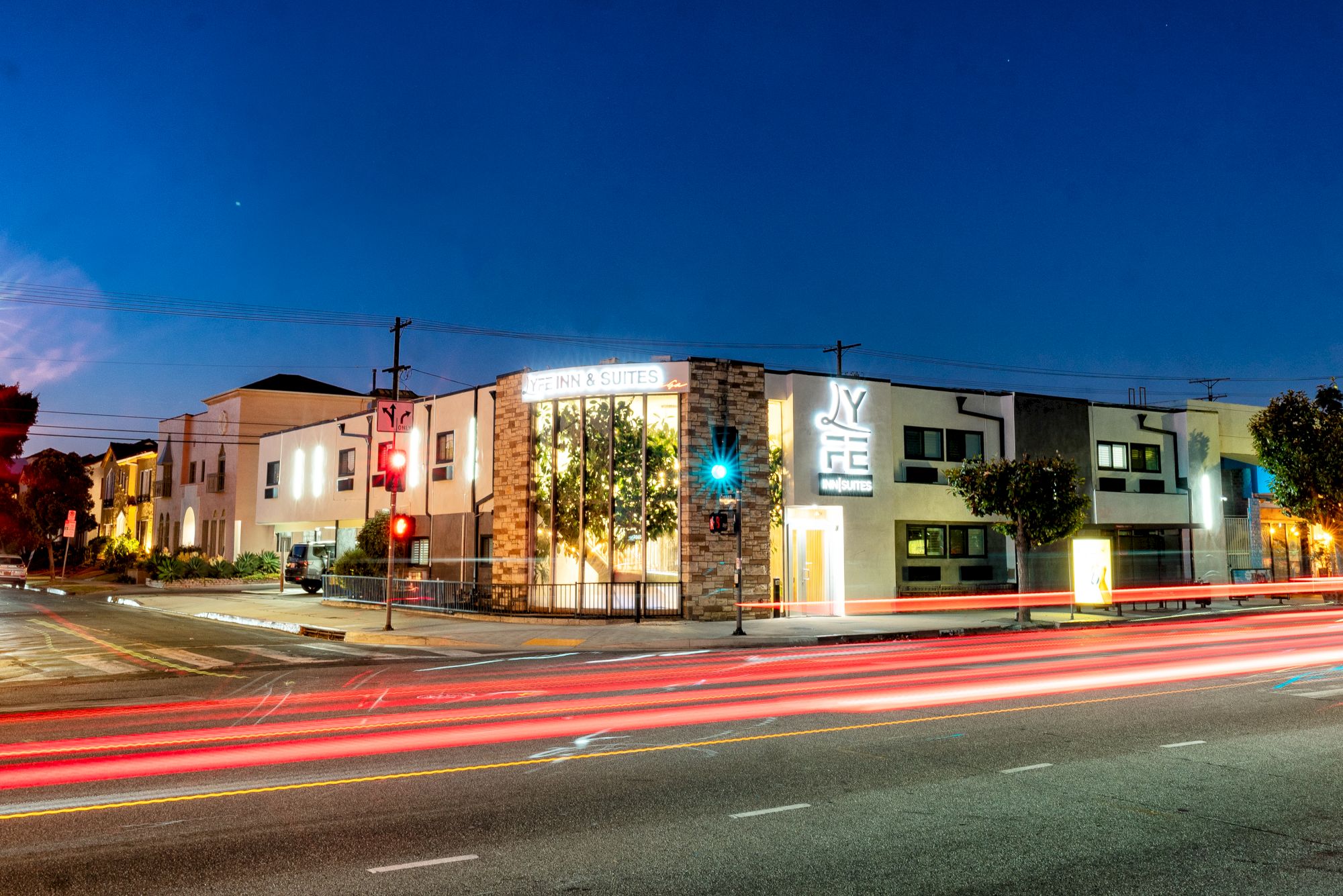 A street at night with light trails from cars, showing a modern building with "ANAHEIM" and "YMCA" signage, and nearby streetlights and trees.