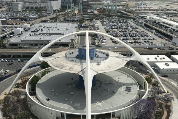 An iconic structure with futuristic design, surrounded by parking lots and buildings, likely part of an airport complex.