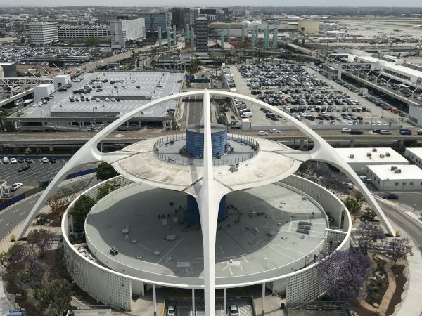 An iconic structure with futuristic design, surrounded by parking lots and buildings, likely part of an airport complex.