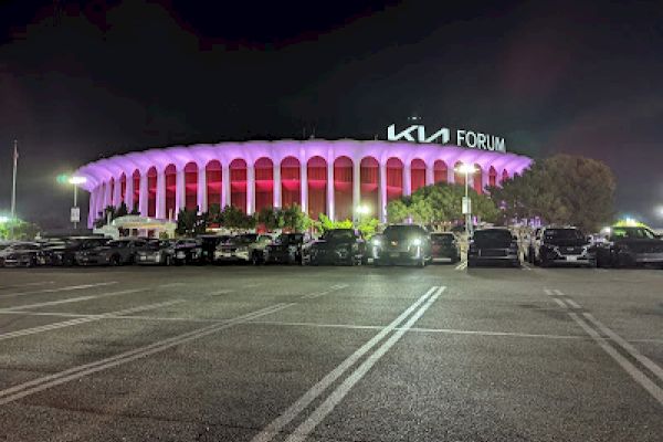 This image shows the KIA Forum, illuminated in purple and red lights at night, with several cars parked in the lot.