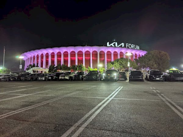 This image shows the KIA Forum, illuminated in purple and red lights at night, with several cars parked in the lot.