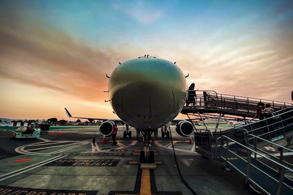 An airplane is parked on the tarmac at an airport during sunset, with a jet bridge connected to it and a clear sky in the background.