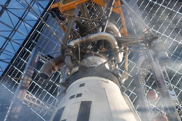 The image shows a view of a rocket engine or spacecraft component inside a large metal framework, with visible pipes and structural elements.