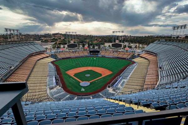 The image depicts an empty baseball stadium with a view of the field and surrounding seating areas. The sky is cloudy in the background.