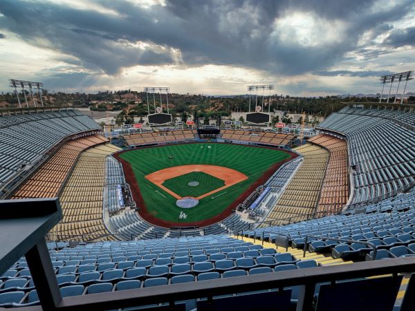 The image depicts an empty baseball stadium with a view of the field and surrounding seating areas. The sky is cloudy in the background.