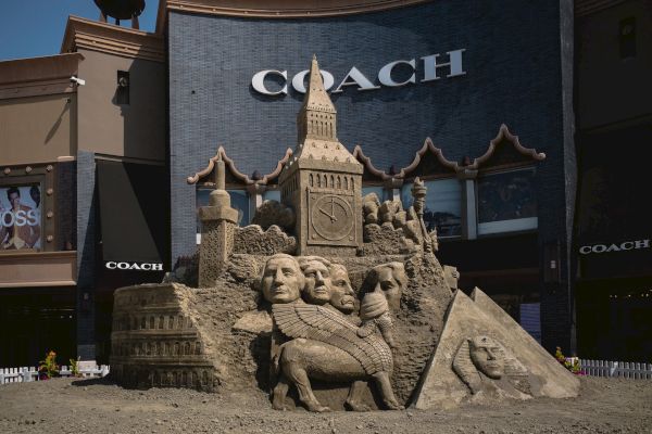 A detailed sand sculpture featuring famous landmarks and historical figures, set in front of a Coach store.