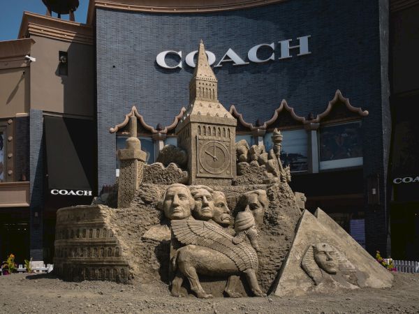 A detailed sand sculpture featuring famous landmarks and historical figures, set in front of a Coach store.