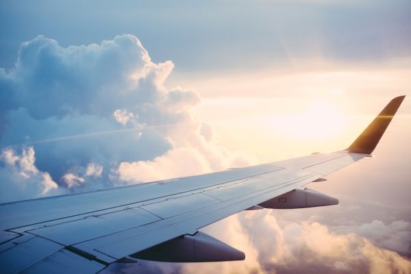 This image shows an airplane wing in flight with clouds and a serene sunlit sky in the background.