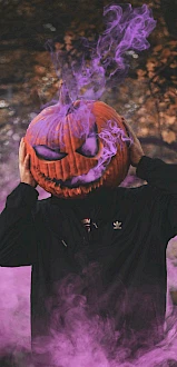 A person in a black hoodie holds a carved pumpkin on their head, with purple smoke emanating from it, surrounded by a misty forest scene.