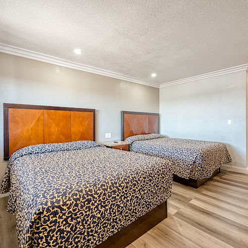 The image shows a hotel room with two beds, patterned bedspreads, and a wooden headboard. The room has modern decor and wooden flooring.