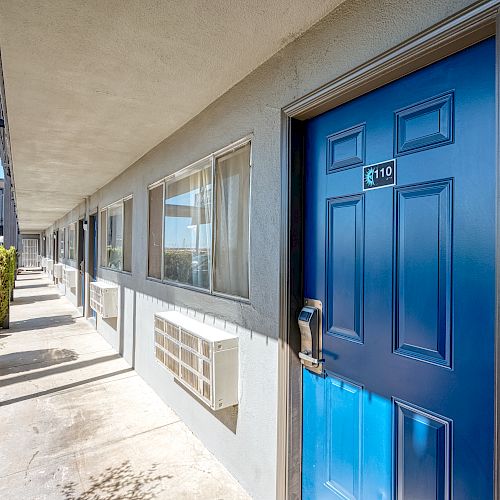 The image shows the exterior of a building with a blue door numbered 119, windows, and air conditioning units along a walkway.