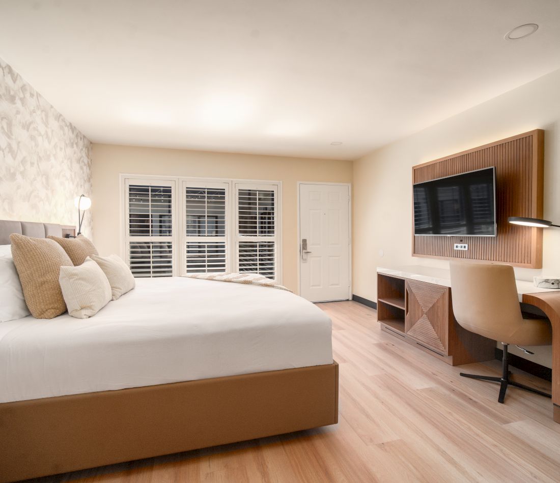 A hotel room with a bed, TV, desk, and window