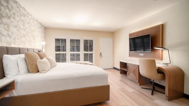 A wide view of a hotel room with a bed, desk, TV, and window.