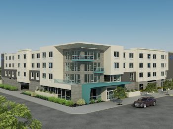 The image shows a modern four-story building with large windows, surrounded by parking spaces and greenery under a clear blue sky.