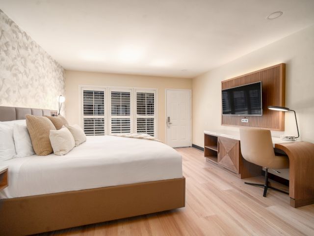 A wide view of a hotel room with a bed, desk, TV, and window.