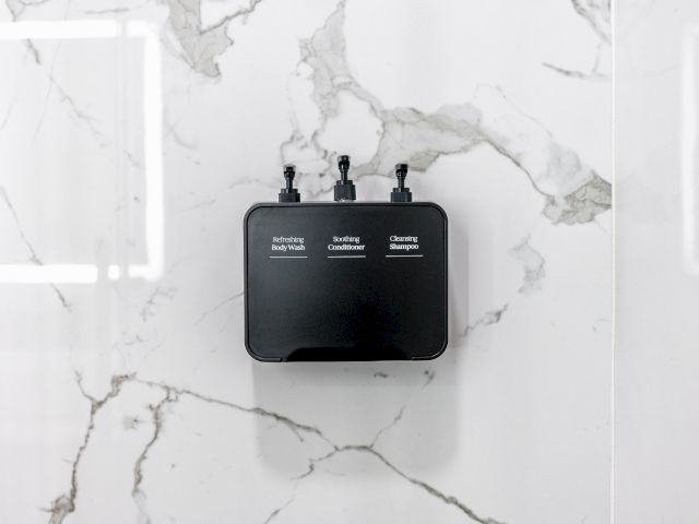 A black wall-mounted dispenser with three bottles for toiletries