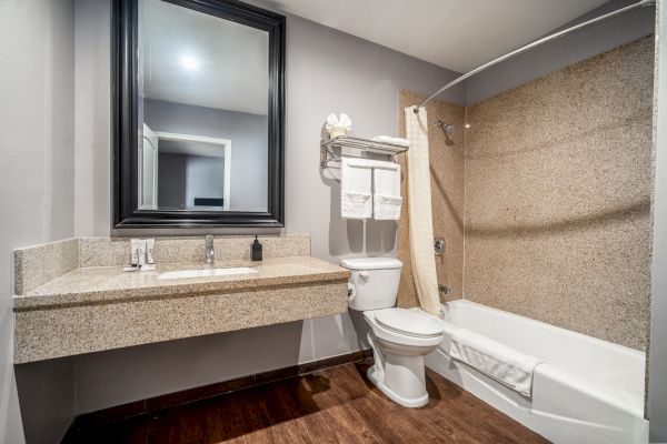 A clean and modern bathroom with a large mirror, sink, toilet, and bathtub, along with neatly arranged towels on the shelf.