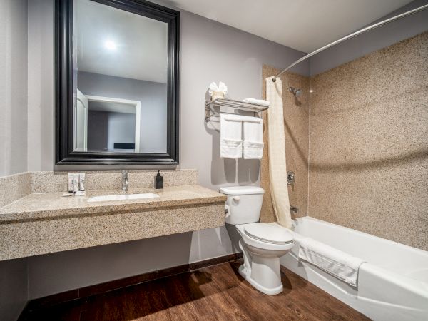 A clean and modern bathroom with a large mirror, sink, toilet, and bathtub, along with neatly arranged towels on the shelf.