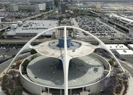 The image shows a modern, futuristic building with a unique architectural design, featuring curved, arch-like structures and located in an urban setting.