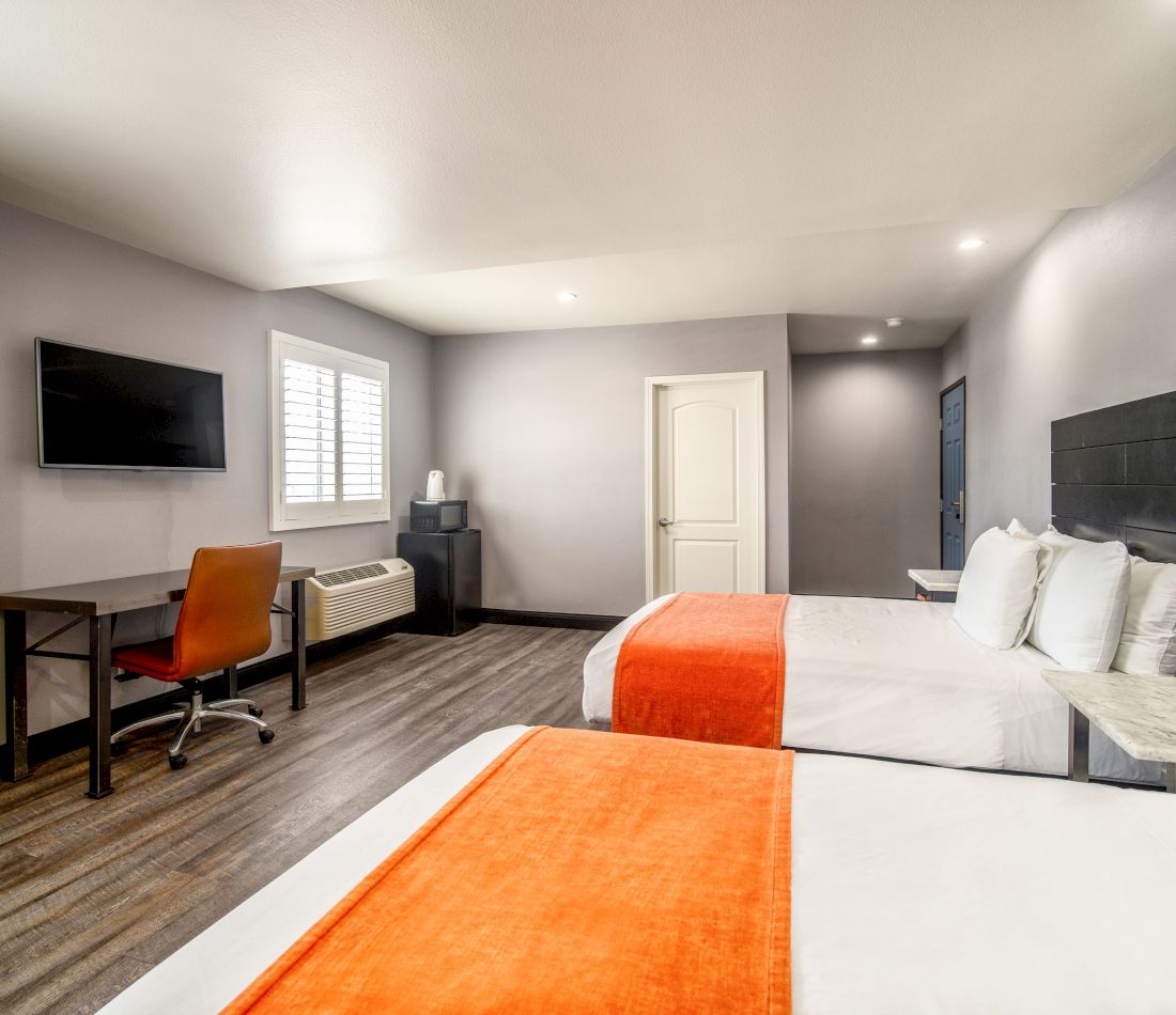 A hotel room with two beds, a desk, and a TV on the wall.