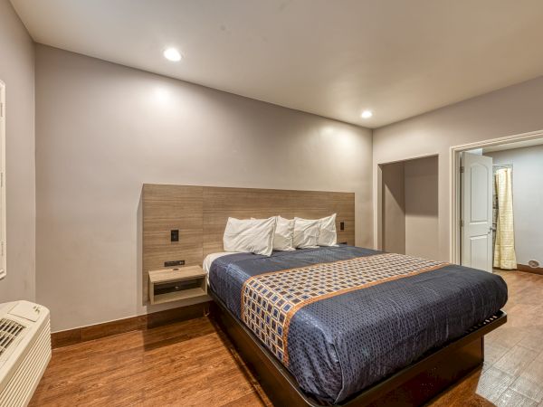 A bedroom with a large bed, white pillows, bedside tables, a door, hardwood flooring, and soft lighting from recessed lights on the ceiling.