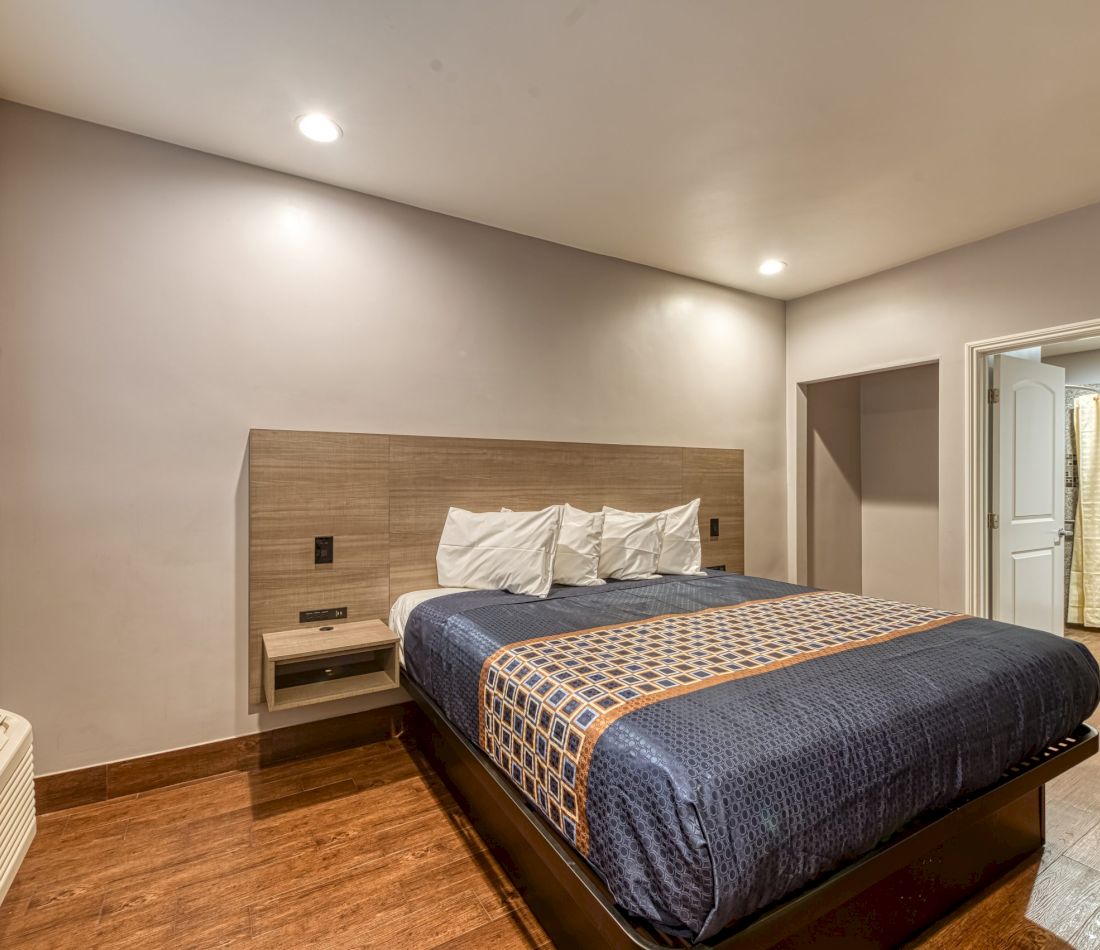 A wide-angle view of a hotel room with a large bed, wooden headboard, and recessed lighting.