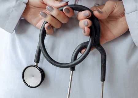 A person wearing a white coat holds a stethoscope behind their back, indicating a medical professional or student.