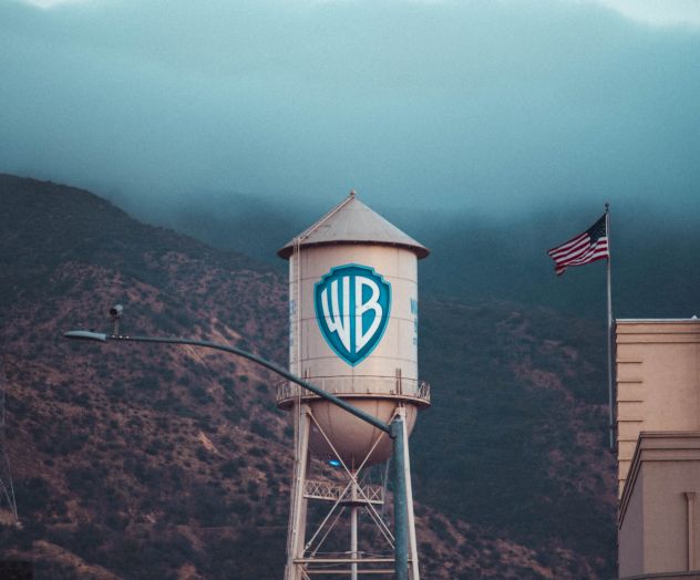 The image shows a Warner Bros. water tower alongside an American flag and street signs reading Olive Ave, with a foggy mountain in the background.