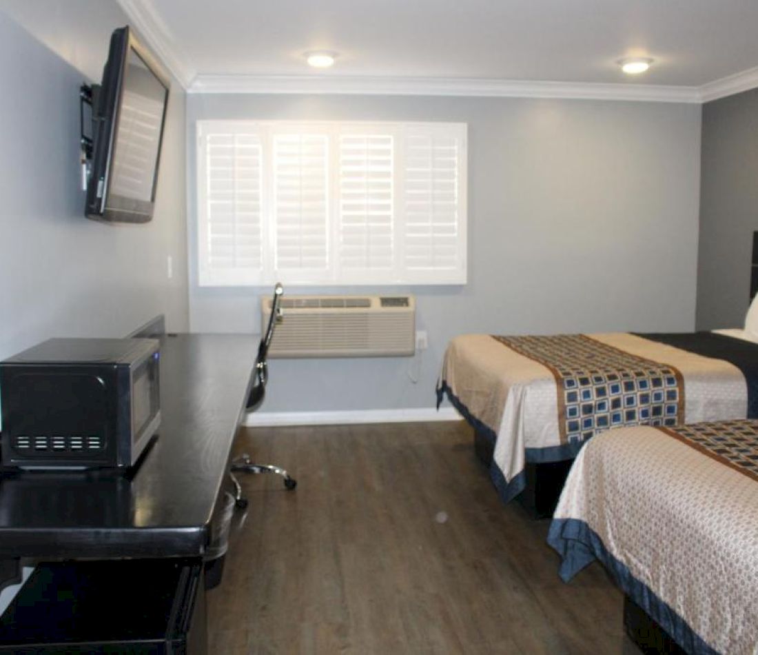 A hotel room with two beds, a desk, a TV, and a microwave.