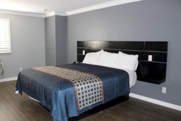 The image shows a modern bedroom with a large bed, blue bedspread, and a dark headboard. The walls are gray with white crown molding.