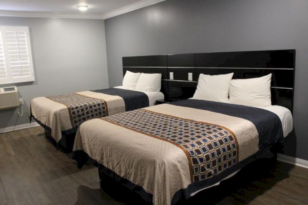 The image shows a hotel room with two double beds, dark blue and beige bedding, an AC unit, and wooden flooring, all under soft lighting.