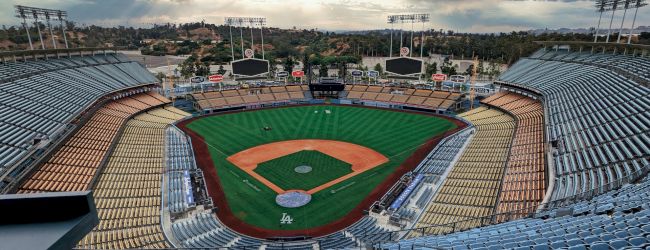 This image shows an empty baseball stadium with a neatly maintained field and a cloudy sky in the background.