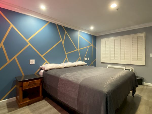 A modern bedroom with a geometric-themed blue accent wall, a double bed with gray bedding, wooden bedside tables, and recessed ceiling lights.